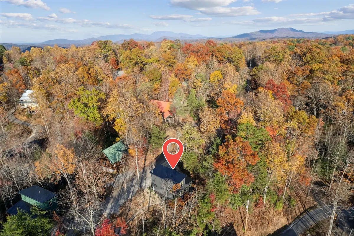 A wide exterior shot capturing the cabin nestled amid vibrant autumn foliage, with distant mountain views and wooded surroundings. The image evokes the spirit of seasonal exploration, outdoor family activities, and the scenic beauty of the Smoky Mountains.