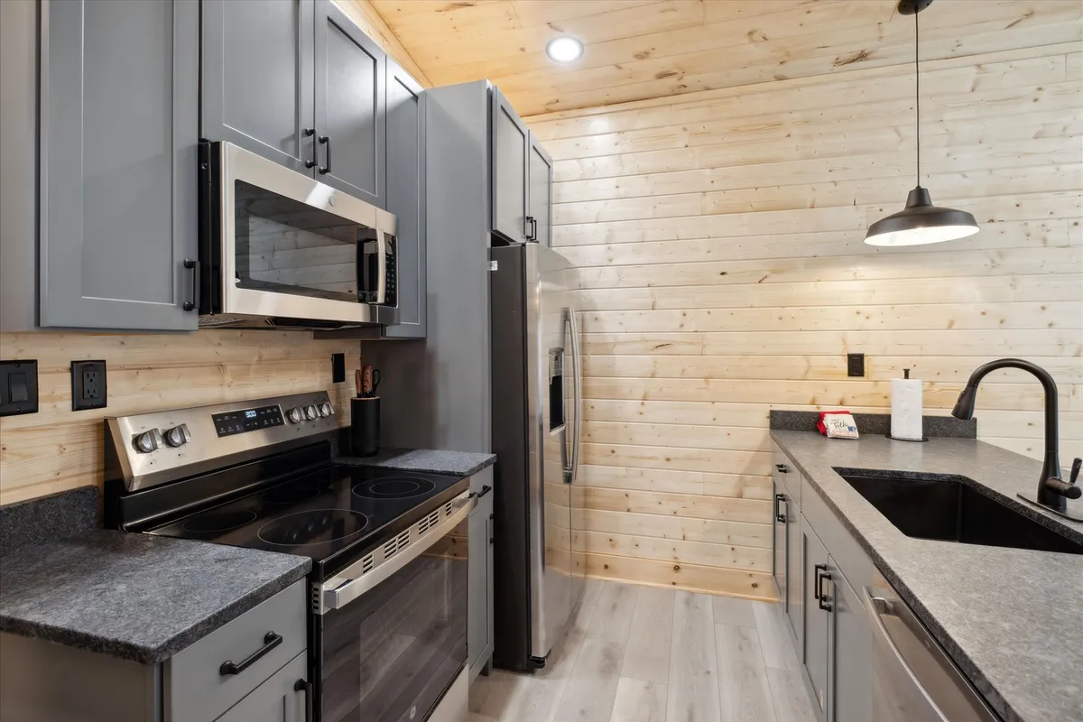 A modern kitchen featuring stainless steel appliances, granite countertops, sleek cabinetry, and wooden wall paneling. The space is designed for efficient meal preparation and group cooking, with contemporary finishes adding a touch of elegance.