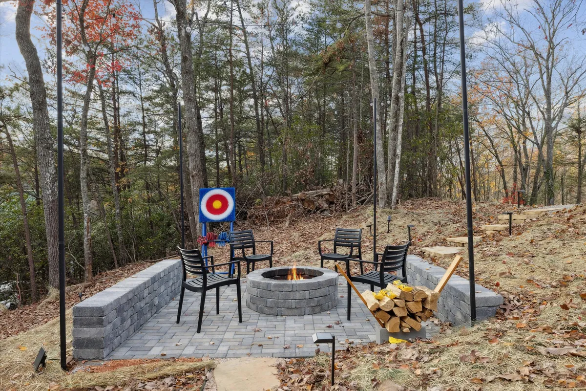 This inviting outdoor area combines a fire pit with ample seating, an archery target, and a tidy stack of firewood. The scene is lively yet cozy, offering spaces for both adventurous activities and relaxing around the fire under the stars.