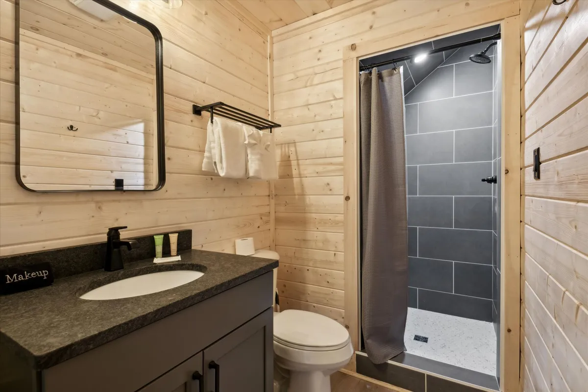 A modern bathroom featuring a sleek vanity with a black countertop, a mirror, a spacious shower area, and a toilet. The ambiance is clean, refreshing, and serene, emphasizing comfort and convenience.